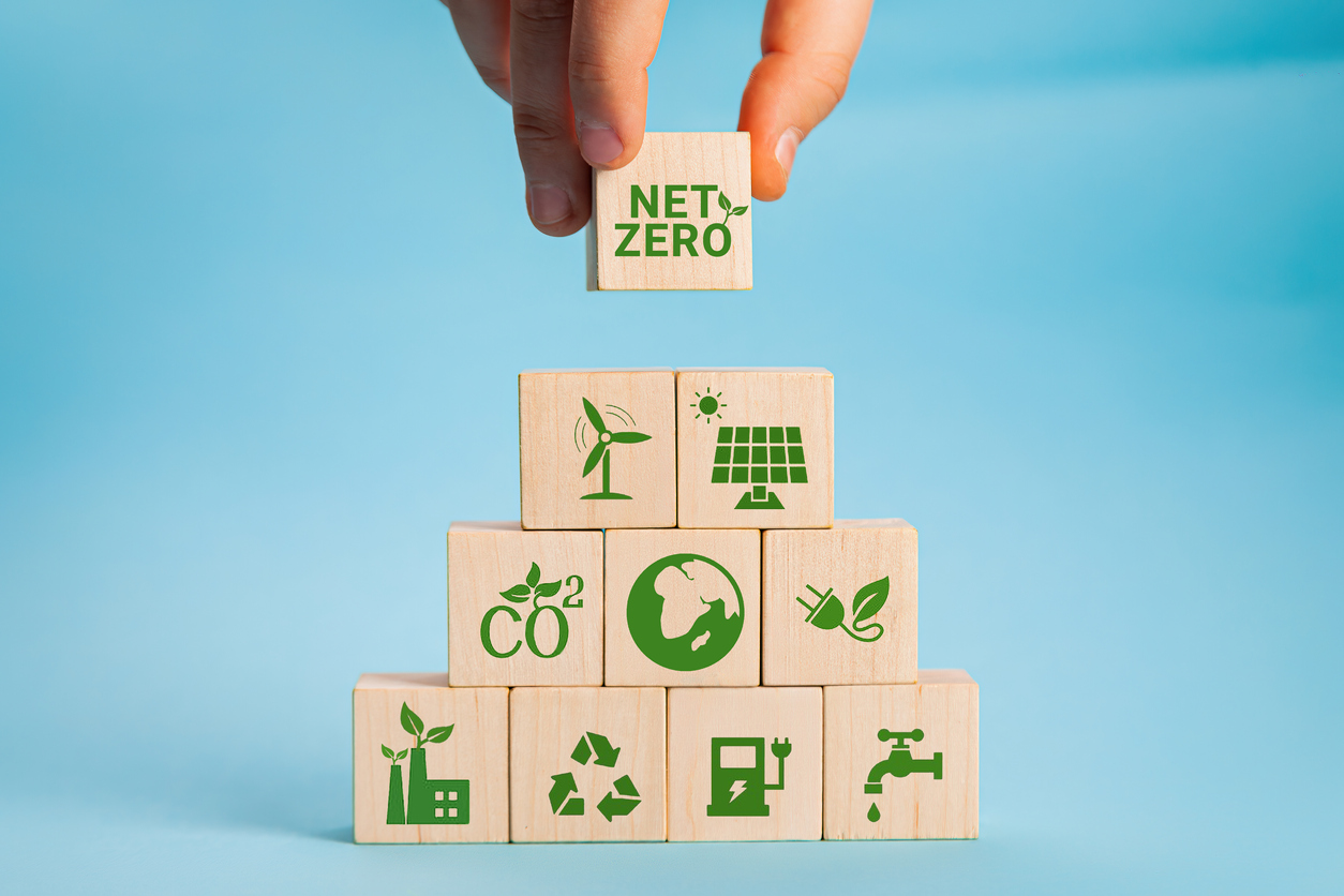 Net zero and carbon neutral concept. Net zero greenhouse gas emissions target. Climate neutral long term strategy. Hand put wooden cubes with green net zero icon and green icon on grey background.